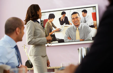 A woman standing in front of a man on a video screen.